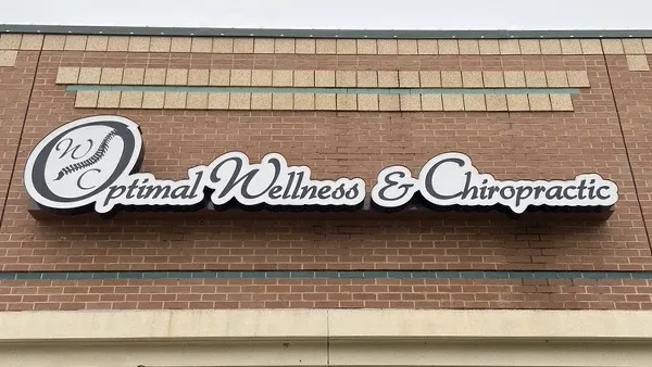 Exterior sign for Optimal Wellness & Chiropractic displayed on a brick building facade.